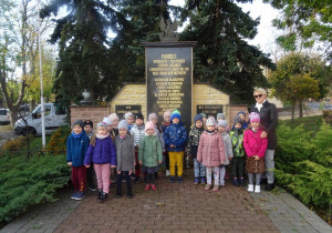 Grupa dzieci z panią Arletą stoi pod pomnikiem poległych podczas II wojny światowe.